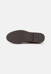 Semelle de chaussure brune avec une surface en caoutchouc texturé, présentant des rainures horizontales pour une meilleure adhérence et un léger talon surélevé. Design simple et fonctionnel.