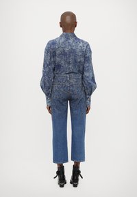 Denim shirt with floral print, high-waisted faded blue jeans, and black ankle boots with bows. Relaxed fit and cropped length.
