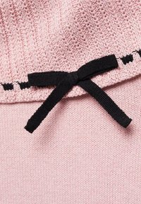 Růžová pletená látka s žebrovaným vzorem a černou mašlí uvázanou u okraje.