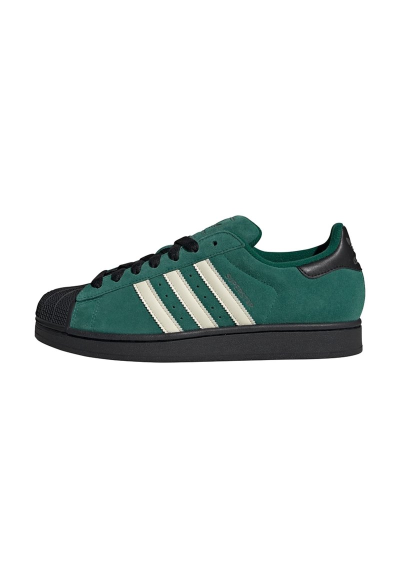 Groene suède sneakers met een zwarte rubberen neuskap, witte strepen, zwarte veters en een gewatteerde kraag. Het ontwerp heeft een gestructureerd oppervlak.