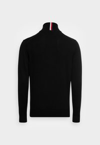 Pull en tricot noir avec un col haut, présentant une rayure rouge et blanche au niveau du col. Texture lisse et silhouette ajustée.