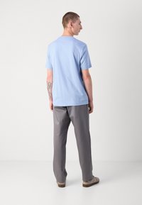 Lyseblå t-skjorte med korte ermer, kombinert med grå bukser. Stoffet ser jevnt ut; t-skjorten har en klassisk rund hals.