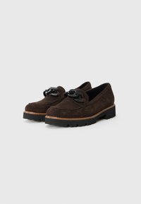 Braune Wildleder-Slipper mit schwarzen Schnürsenkeln, stabiler schwarzer Gummisohle, abgerundetem Zehenbereich und kontrastierendem hellen Nähten entlang der Kante.
