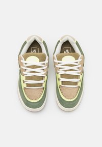 Zapatillas de ante verde y beige con cordones blancos, acentos amarillos y un logo redondo en la lengüeta; paneles texturizados y detalles perforados.