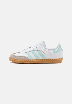 Baskets Adidas Samba blanches et bleu clair avec semelle en caoutchouc et bout en daim beige, vues de côté sur fond blanc.