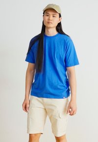 T-shirt en coton bleu à manches courtes, associé à un short cargo beige avec plusieurs poches. Design simple, couleur unie, coupe décontractée.