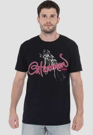 Man wearing black t-shirt with drawing of gloved hand and the word Catwoman in red script with a small Batman logo.