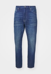 Jeans de denim azul oscuro con corte recto, que cuentan con un cierre frontal de botón y cremallera, cinco bolsillos y un ligero desgaste a lo largo de las piernas.