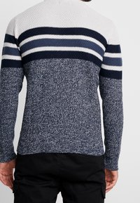 Knitted pullover with a textured navy and white design, featuring horizontal stripes in varying shades of blue on the upper back.