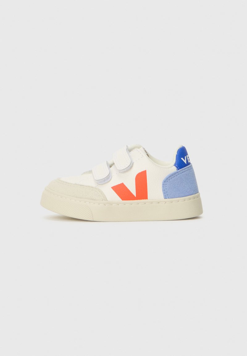 Hvite sneakers med borrelås, med en rød 'V' logo og blå semsket skinn detaljer på hælen. Gummisåle, avrundet tå og teksturert overflate.