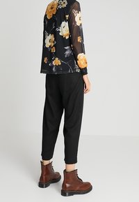 Schwarze durchsichtige Bluse mit floralen Mustern in Orange, kombiniert mit schwarzen, schmal geschnittenen Hosen und braunen Schnürstiefeln, die einen geschichteten und strukturierten Look präsentieren.
