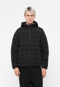 Doudoune noire avec capuche, présentant un design matelassé, une fermeture éclair à l'avant et des poignets côtelés. Fabriquée en matériau lisse et léger.