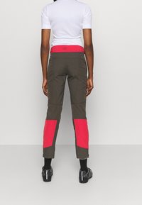 Spodnie outdoorowe w ciemnozielonym kolorze z jasnoróżowymi panelami bocznymi. Posiadają dopasowany krój oraz pas w talii z detalem w postaci logo.