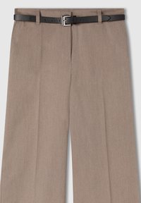 Beżowe spodnie o dopasowanym kroju z fałdami z przodu oraz wąski czarny skórzany pasek z prostokątną srebrną klamrą.