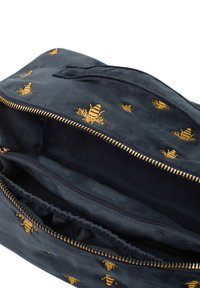 Černá látková taška se zlatou výšivkou včely. Má zipové uzavírání, elastickou kapsu uvnitř a hladký povrch.