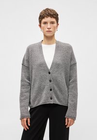 Cardigan cinza com decote em V, mangas longas e cinco botões frontais. Feito de material suave, com um corte solto e uma barra ligeiramente arredondada.