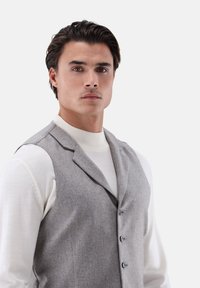 Grau, maßgeschneiderte Weste aus Wollmischung, mit Reverskragen, drei Knöpfen und subtiler Textur, getragen über einem cremfarbenen Rollkragenpullover.