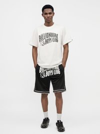 Νεαρός άνδρας που φοράει λευκό μπλουζάκι Billionaire Boys Club, μαύρα σορτς με το ίδιο λογότυπο, λευκές κάλτσες και μαύρα αθλητικά παπούτσια.