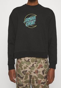 Black cropped sweatshirt with a round neckline featuring a turquoise and yellow "Santa Cruz" logo in the center. Cotton blend material.