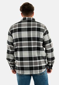 Camicia in flanella a quadri grigia e nera, con una texture morbida, colletto con bottoni e maniche lunghe, mostrata di spalle.