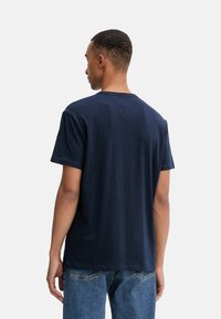 Camiseta de algodón azul marino con cuello redondo, mangas cortas y un corte relajado. Presenta costuras dobles y un diseño en la parte posterior sin etiqueta.