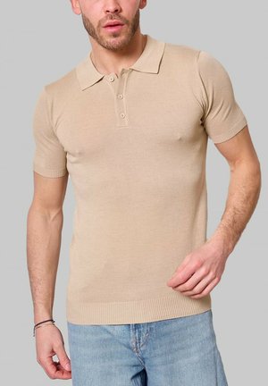 Polo t-shirt à manches courtes en tricot de couleur tan, doté d'un col classique, d'une patte de boutonnage à trois boutons et de poignets côtelés. Porté avec un jean bleu clair.