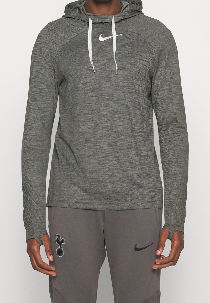 Haut à capuche gris à manches longues en tissu texturé, avec un logo Nike blanc sur la poitrine et des cordons de serrage réglables sur la capuche.