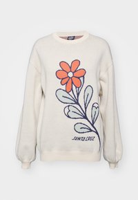 Pull de couleur crème à manches longues, présentant un motif floral en orange et vert, avec le texte "SANTA CRUZ" en bleu. Texture en tricot.