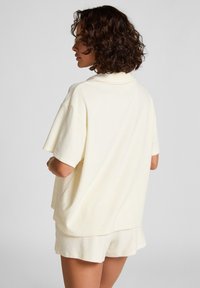 Light cream, short-sleeve top with a relaxed fit, soft texture, and a subtle collar, paired with matching shorts.