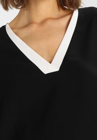 Top nero a V con un bordo bianco a contrasto lungo il collo, che presenta una texture liscia e una vestibilità comoda.
