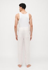 Pantalones de lino color beige claro con un corte relajado, que cuentan con bolsillos traseros y una superficie ligeramente texturizada, combinados con una camiseta sin mangas blanca.