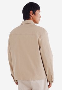 Beige, lichte jas met een kraag, geknoopte manchetten en een rechte snit. Kenmerkt zich door een effen textuur met een schone, minimalistische uitstraling.