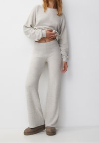 Conjunto de lounge de color gris claro hecho de tela suave; consta de un top corto de manga larga y pantalones de pierna ancha de talle alto con una textura suave.