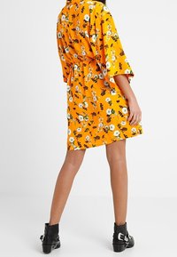Floral kimono dress in bright orange with black and white flowers, tied at the waist. Features wide sleeves and a relaxed fit. Black ankle boots.
