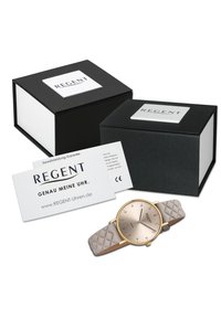 Montre dorée avec un cadran rond et métallique, dotée d'index horaires saillants. Elle possède un bracelet en silicone texturé gris clair. Comprend des boîtes d'emballage noires.