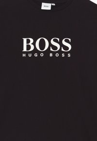 Camiseta de algodón negra con gran logo blanco "BOSS" y el texto más pequeño "HUGO BOSS" debajo. Diseño de cuello redondo con mangas cortas.