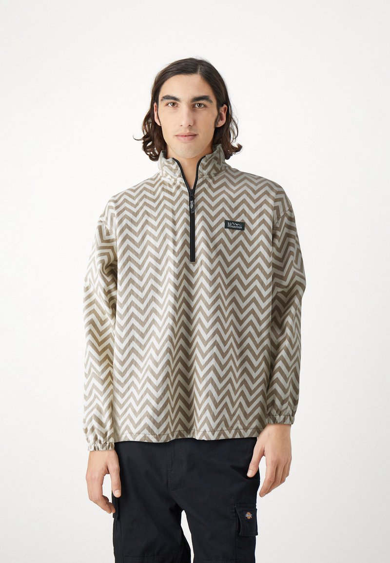Pullover jacket in beige with a zigzag pattern, quarter-zip front, elasticated cuffs, and logo patch on the left chest. Textured fabric.