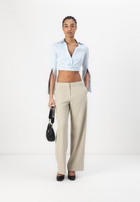 Lyseblå cropped skjorte med åpne ermer, beige vide bukser, svart handbag, og svarte hæler. Glatt stoff, rene linjer, moderne passform.