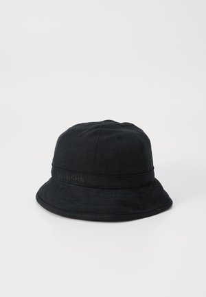 Juodas medvilninis kibiro skrybėlė su plačiu kraštu, pasižyminti tekstūruota apdaila ir iškilniu "Calvin Klein" logotipu ant juostos.