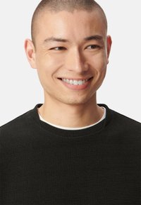 Czarny sweter o fakturze z okrągłym dekoltem. Materiał ma wzór w wafle, spod którego wystaje biały podkoszulek przy kołnierzu.