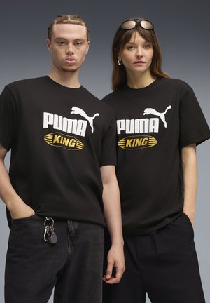 Black cotton t-shirts featuring a white Puma logo and bold "PUMA KING" text in gold. Worn with dark denim and relaxed trousers.