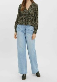 Černá květinová zavinovací halenka s dlouhými rukávy a volánem na lemu, kombinovaná s vysokými světle modrými širokými džínami a černými kotníkovými botami.