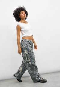 Hvit cropped topp med blonder, kombinert med løse, mønstrede grå bukser med abstrakte design og sidelommer. Svarte sko fullfører antrekket.