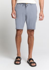Lichtgrijze shorts van zachte stof, met een tailleband met trekkoord en een enkele voorkant zak met een gele accent. Gecombineerd met zwarte sandalen.