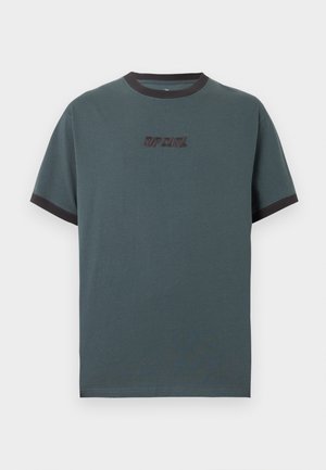 Tânăr cu păr creț, purtând un tricou Rip Curl verde închis cu guler și margini negre la mâneci și pantaloni scurți cargo negri.