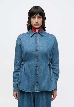Denimskjorte i lyseblå, med krage, knappestolpe, innsnevret midje med knyting og en kontrasterende rød indre krage.