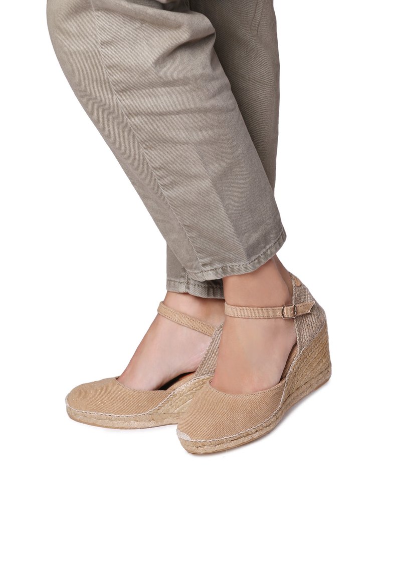Béžové espadrilové wedges se strukturovaným plátěným svrškem, nastavitelným popruhem kolem kotníku a středovou částí z pleteného lana. Silueta má kulatou špičku.