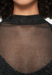 Top nero in rete con scollo alto, caratterizzato da una texture trasparente e un leggero scintillio. Tessuto a maglia liscia con design aderente.