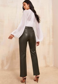 Bluză albă cu mâneci bufante, împodobită cu buline, asociată cu pantaloni din piele ecologică de culoare verde măslin, cu talie înaltă. Sandale maro cu toc completează ținuta.