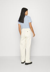 T-shirt azzurro in cotone con maniche corte abbinato a pantaloni bianchi a vita alta e gamba larga, insieme a sneaker nere spesse.
